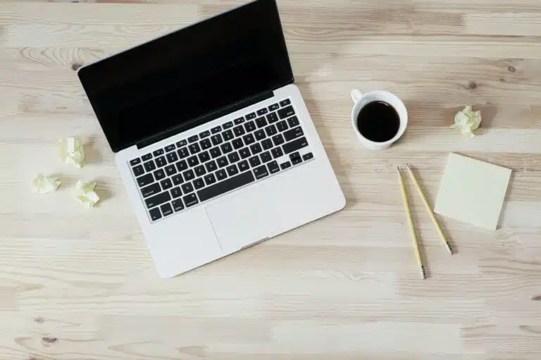 Table with Laptop and Coffee next to Small Sticky Note Pad and Crumpled Papers